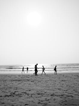 Black and white photo of people walking on Goa beach at sunset, India.