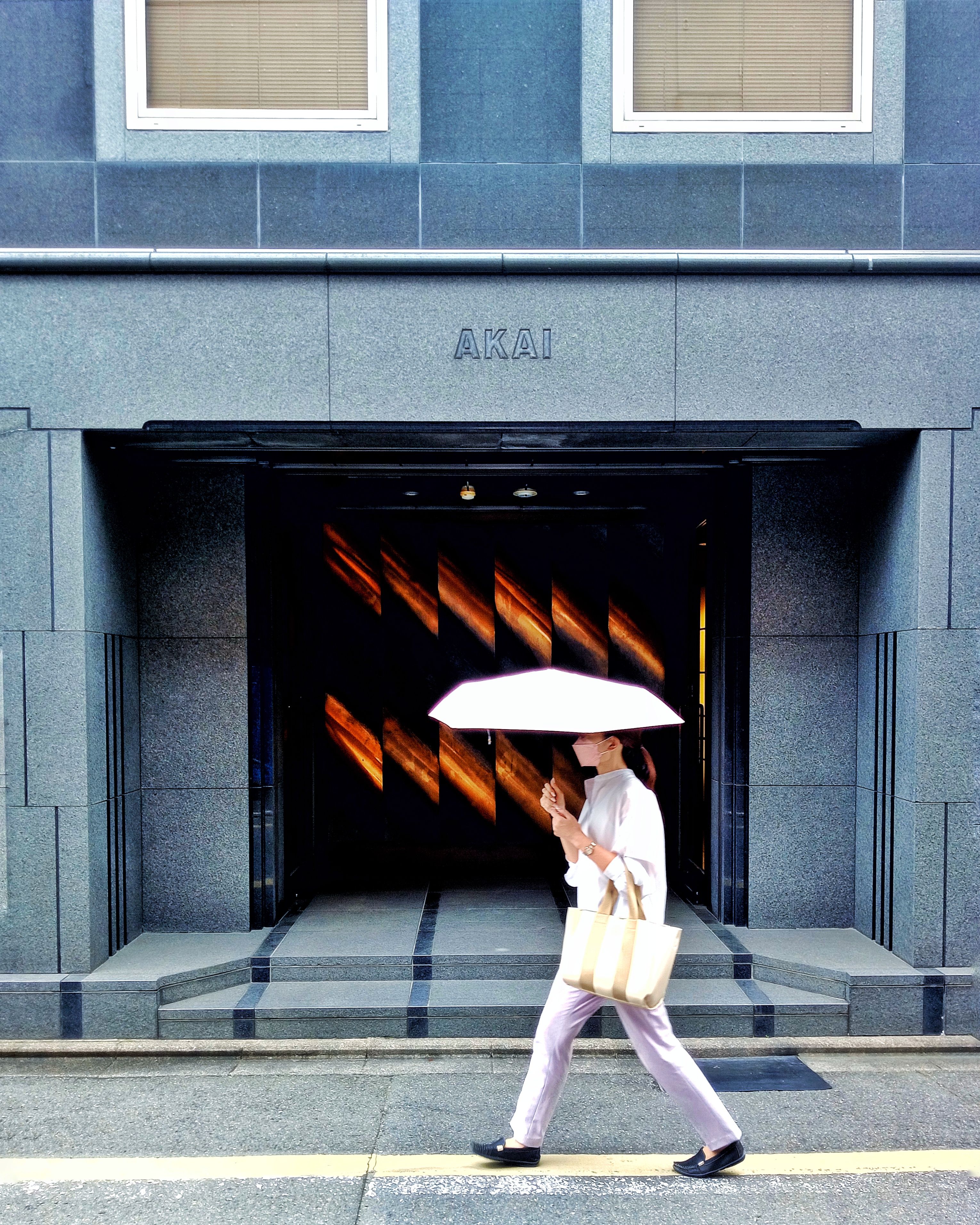 A woman holding an umbrella walks by a stylish building entrance.