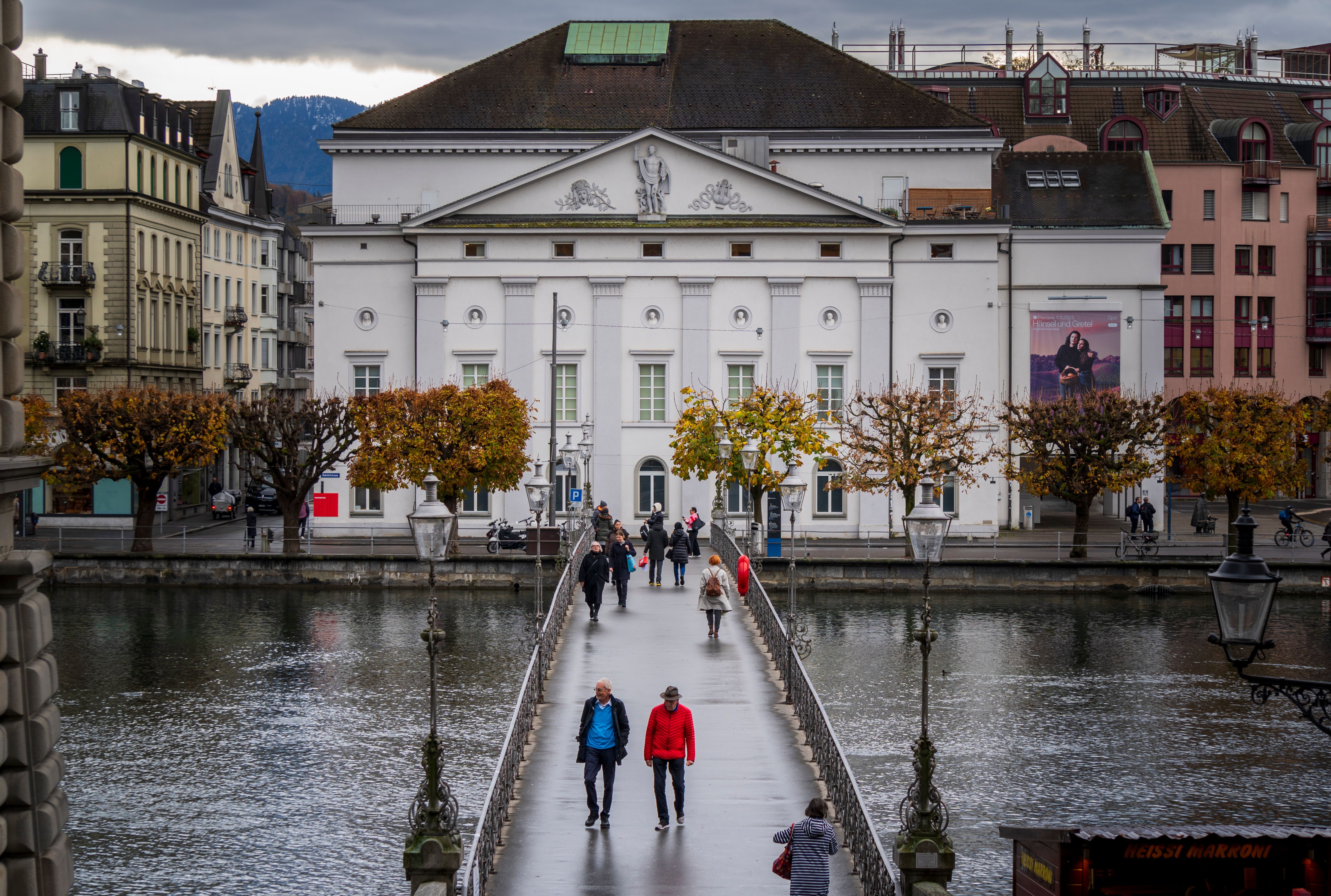 Scenic view of a bridge over a river in Lucerne, Switzerland, with people walking under cloudy skies.