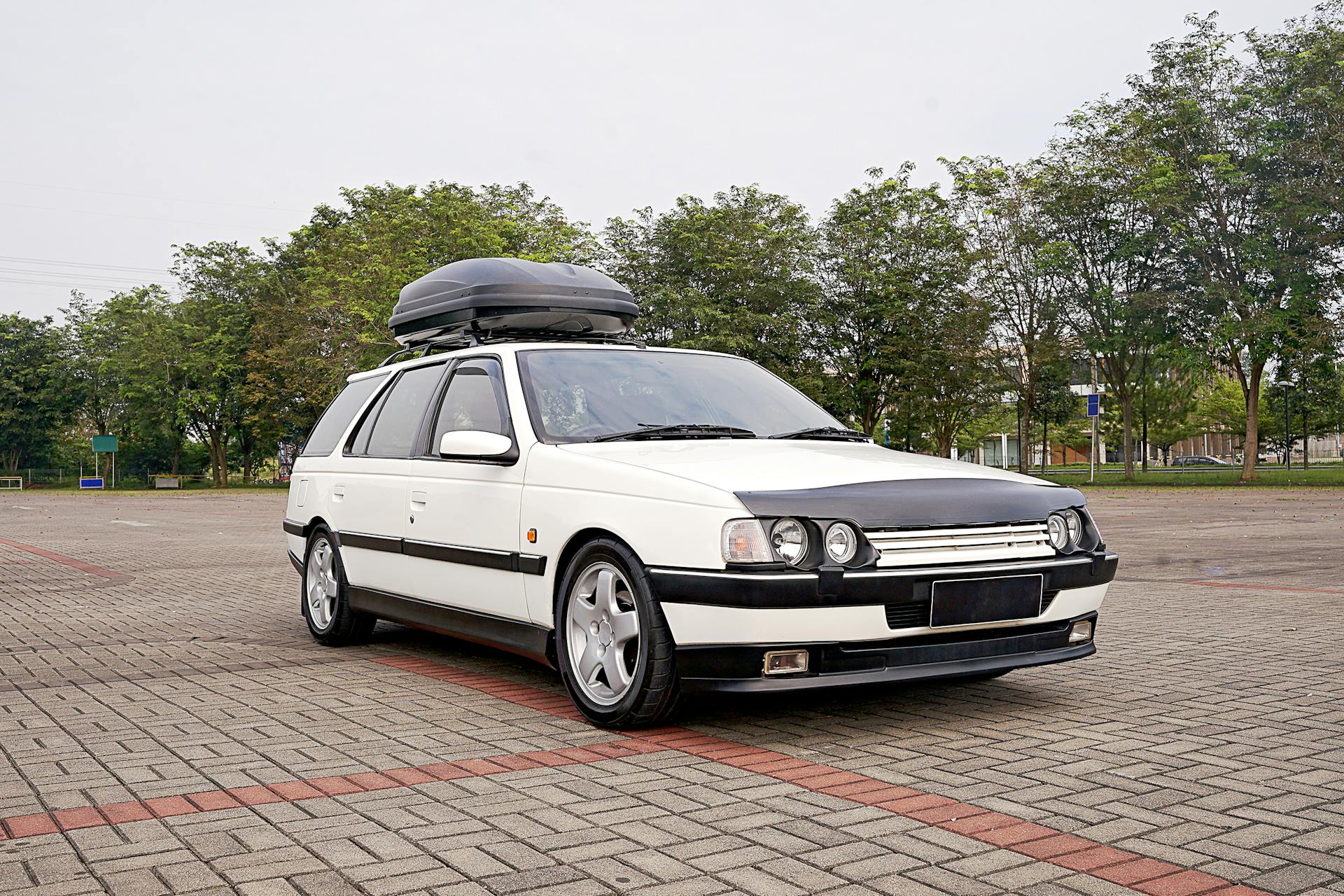 Classic white station wagon with rooftop cargo box parked outdoors in Jakarta.