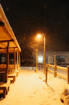 A cozy winter night scene with warm street lights illuminating the falling snow.