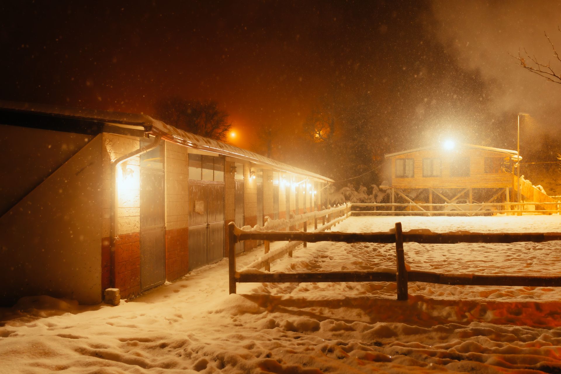 A cozy barn illuminated on a snowy night, featuring warm glowing lights and snow-covered ground.