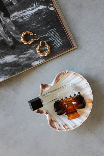 Flat lay of a perfume bottle, shell, and accessories for a stylish, minimalist look.