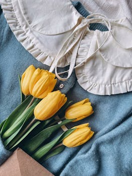 Stylish flat lay of yellow tulips on a blue fabric with a white ruffled collar, creating a vintage aesthetic.