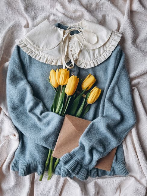 Soft blue sweater holding yellow tulips with an envelope, creating a cozy and elegant vibe.