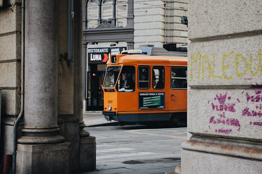 一辆老式橙色电车穿过历史悠久的城市街道，街道两旁建筑林立，还有意大利餐厅的招牌
