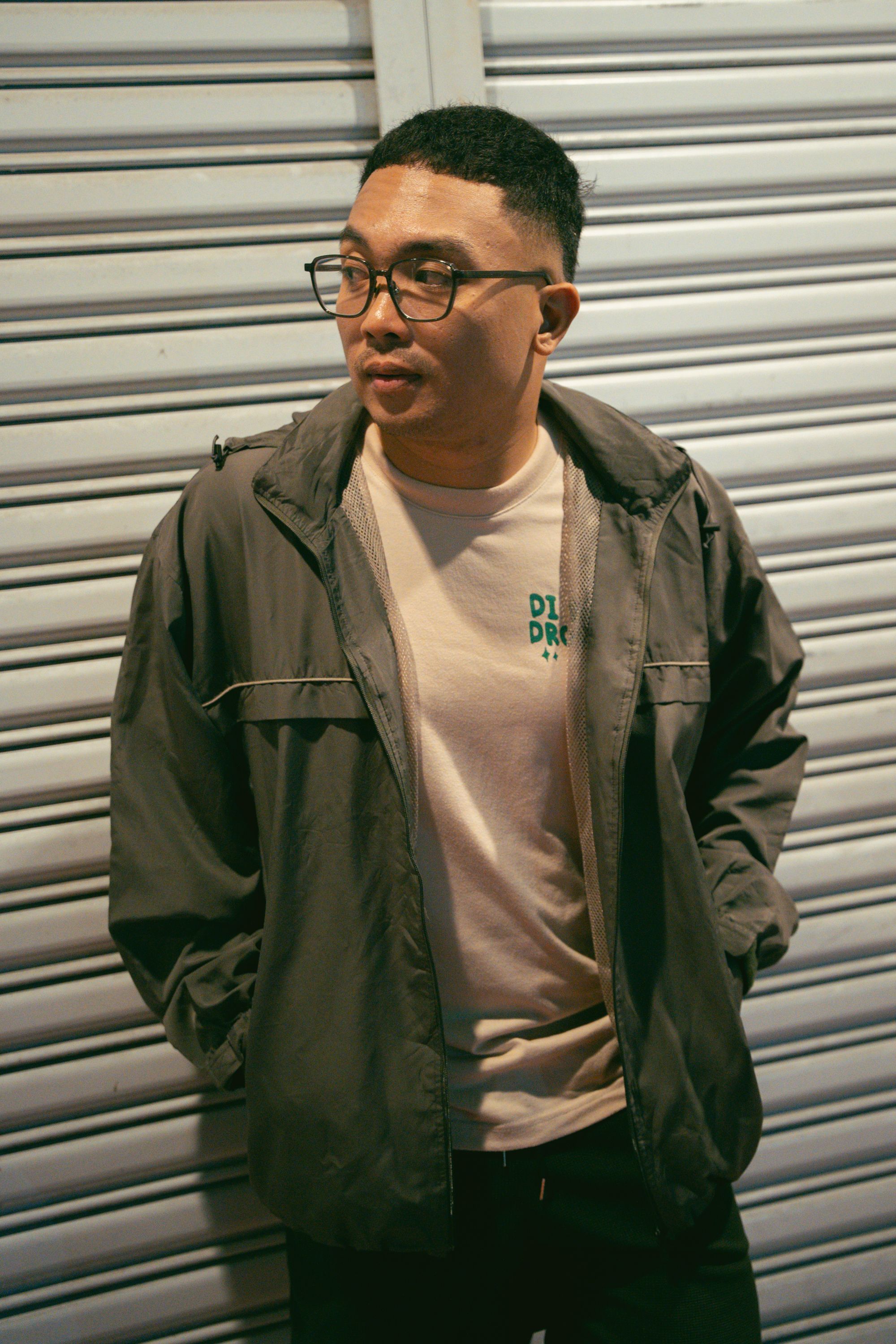 Stylish man wearing a green jacket standing in front of metal shutters, exuding casual urban vibes.