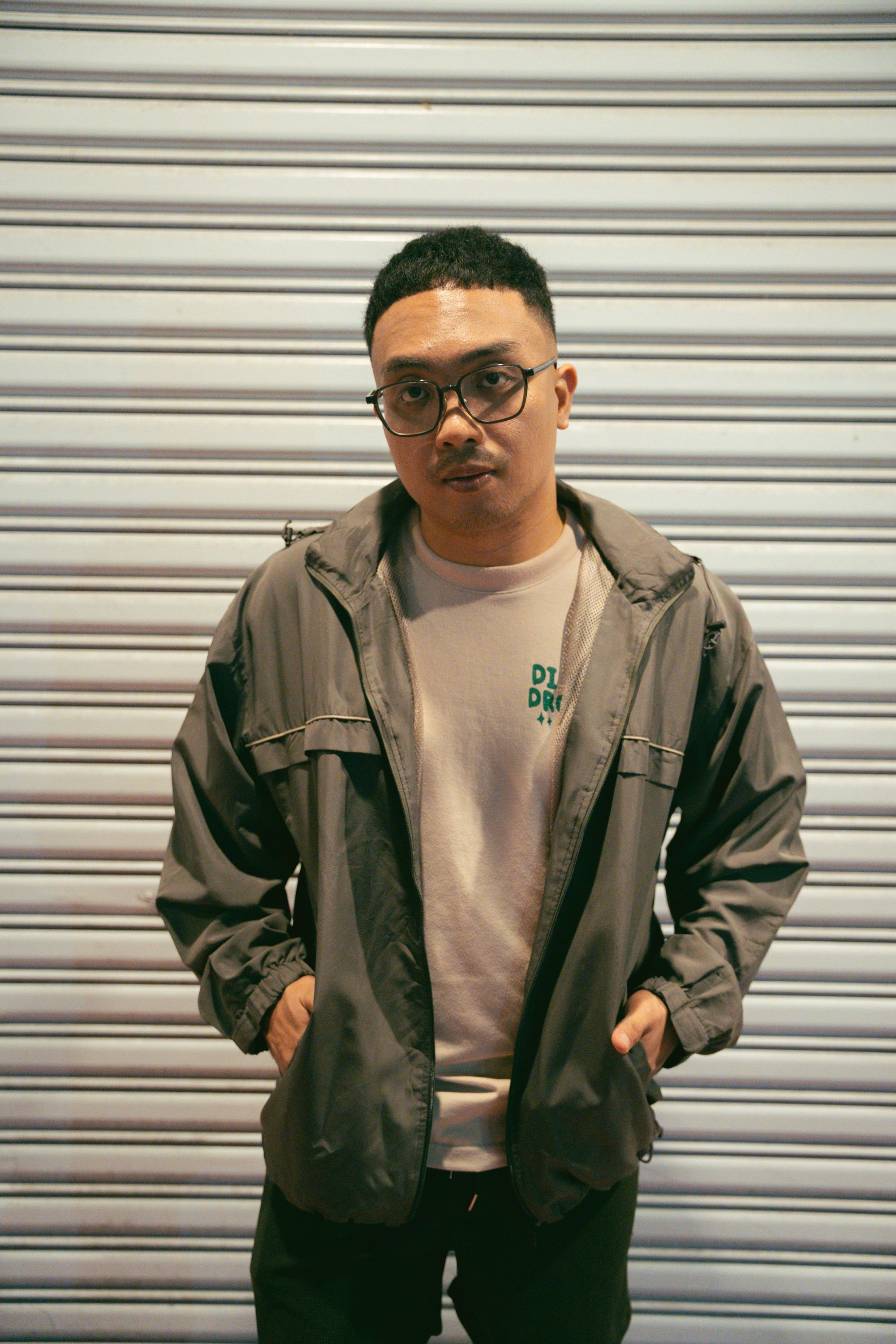 A young adult man standing against a metal shutter in casual attire. Urban setting.