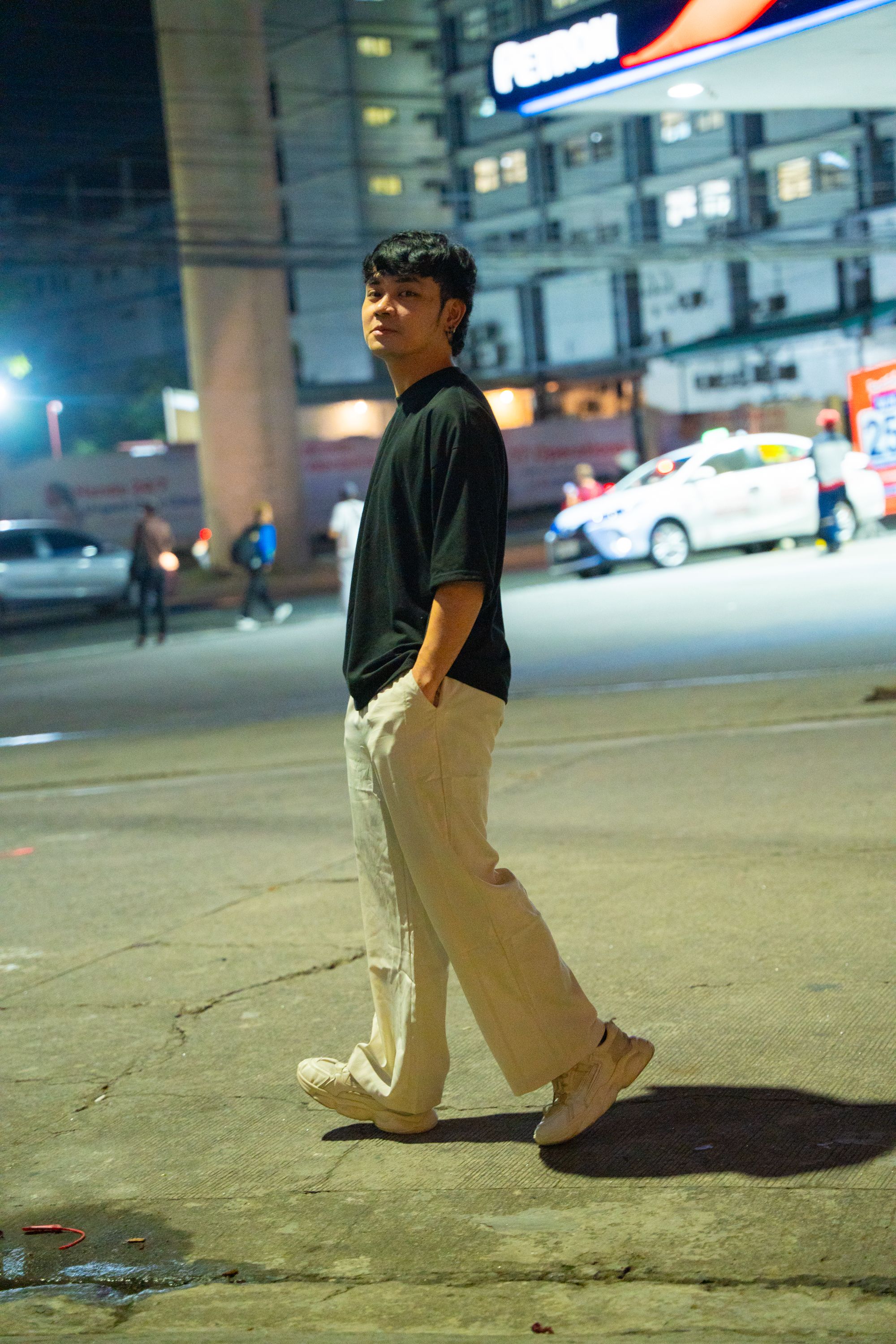A young man in casual clothing walking on a city street at night.