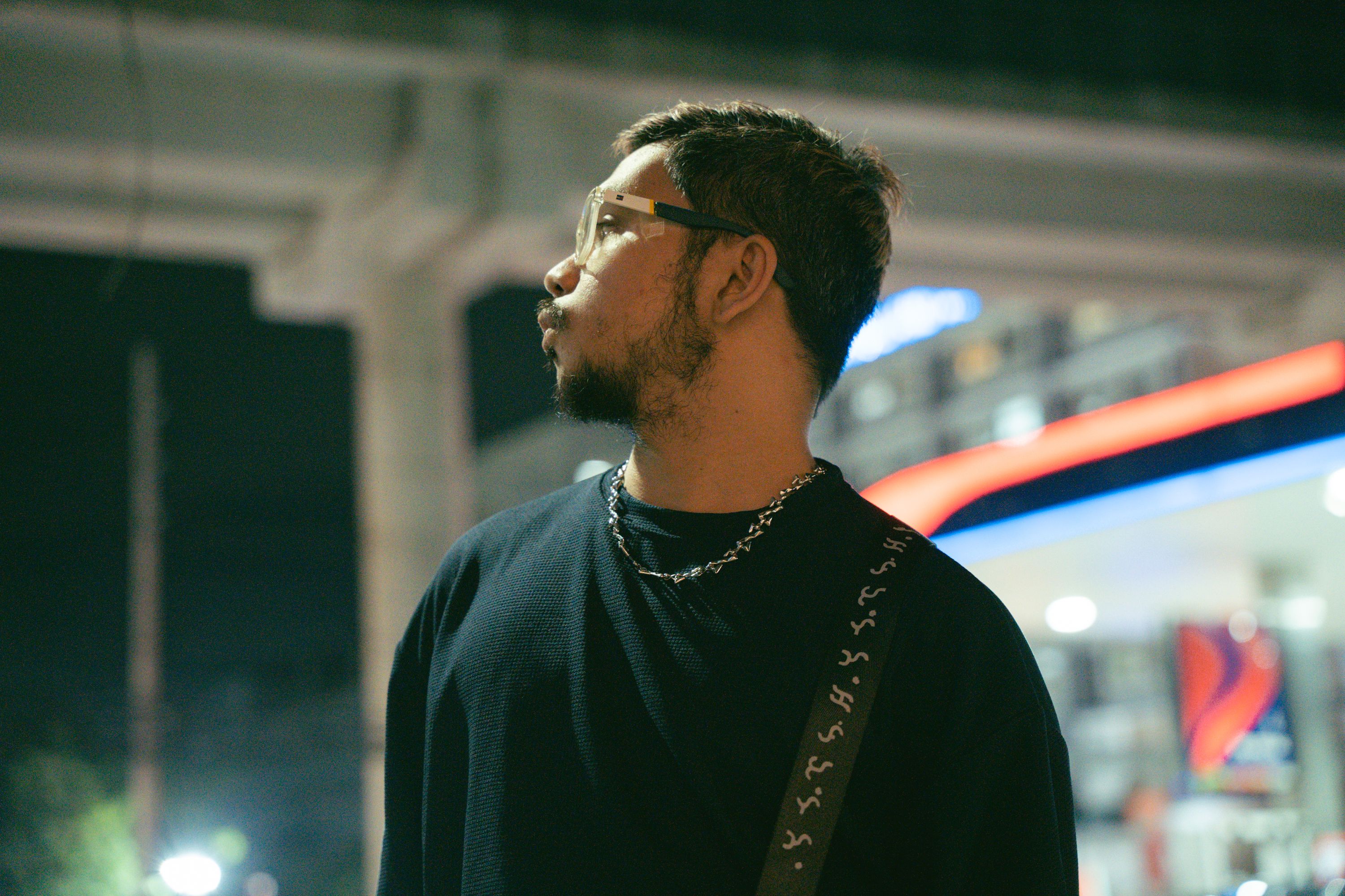 A man looks thoughtfully into the distance under city lights at night.