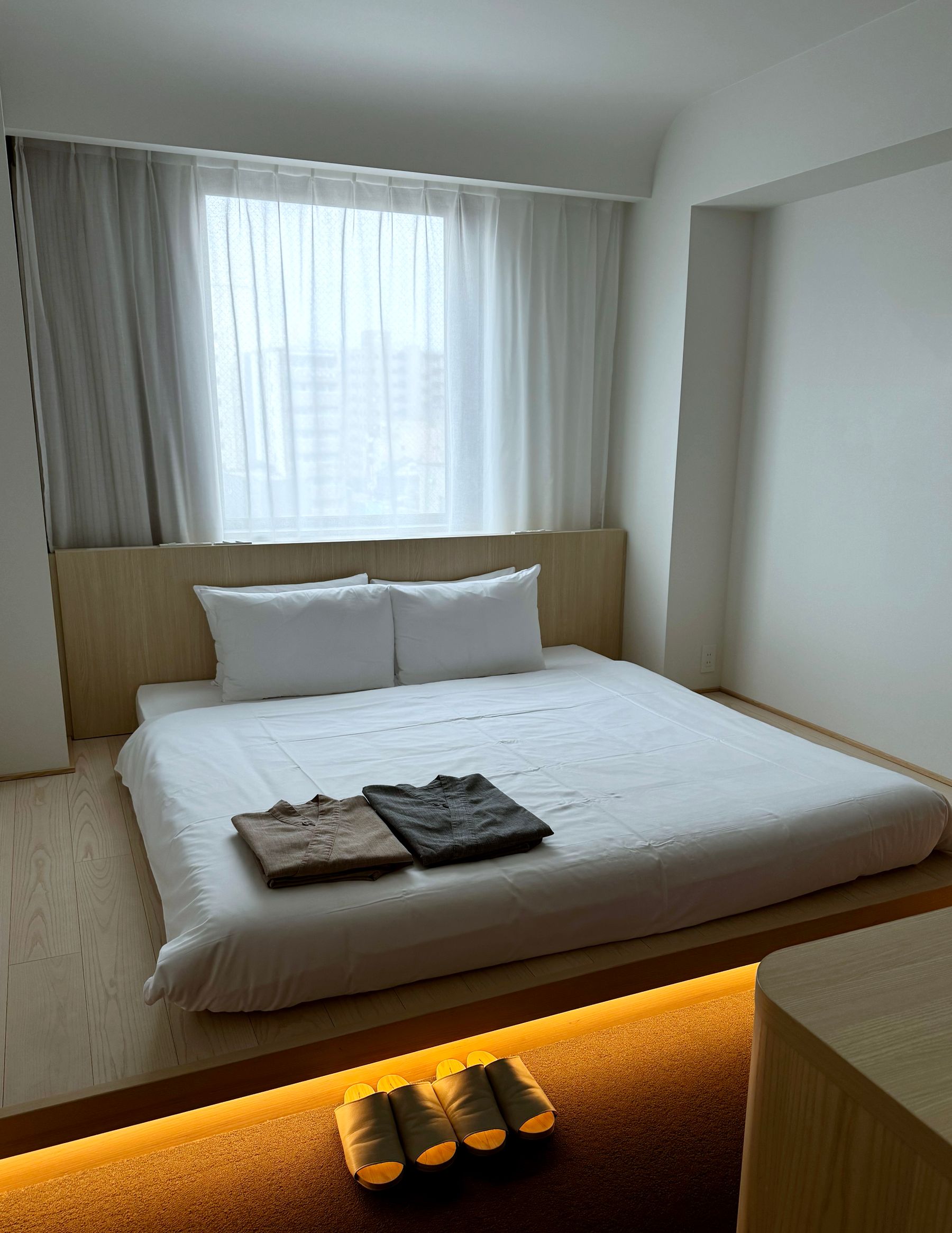 Modern Japanese bedroom with two low western beds, beige upholstery, dark slatted ceiling and compact seating