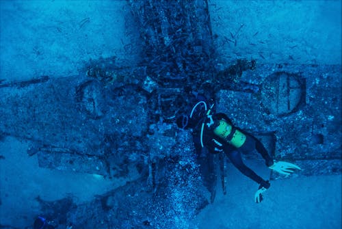 Top view of unrecognizable person in wetsuit inspecting rough remains of sunken plane on bottom of sea