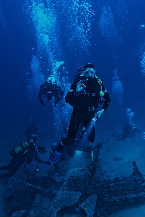 Free A group of scuba divers exploring a submerged shipwreck in the ocean. Stock Photo