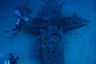 From above anonymous divers swimming and examining remains of aged sunken aircraft on bottom of blue sea