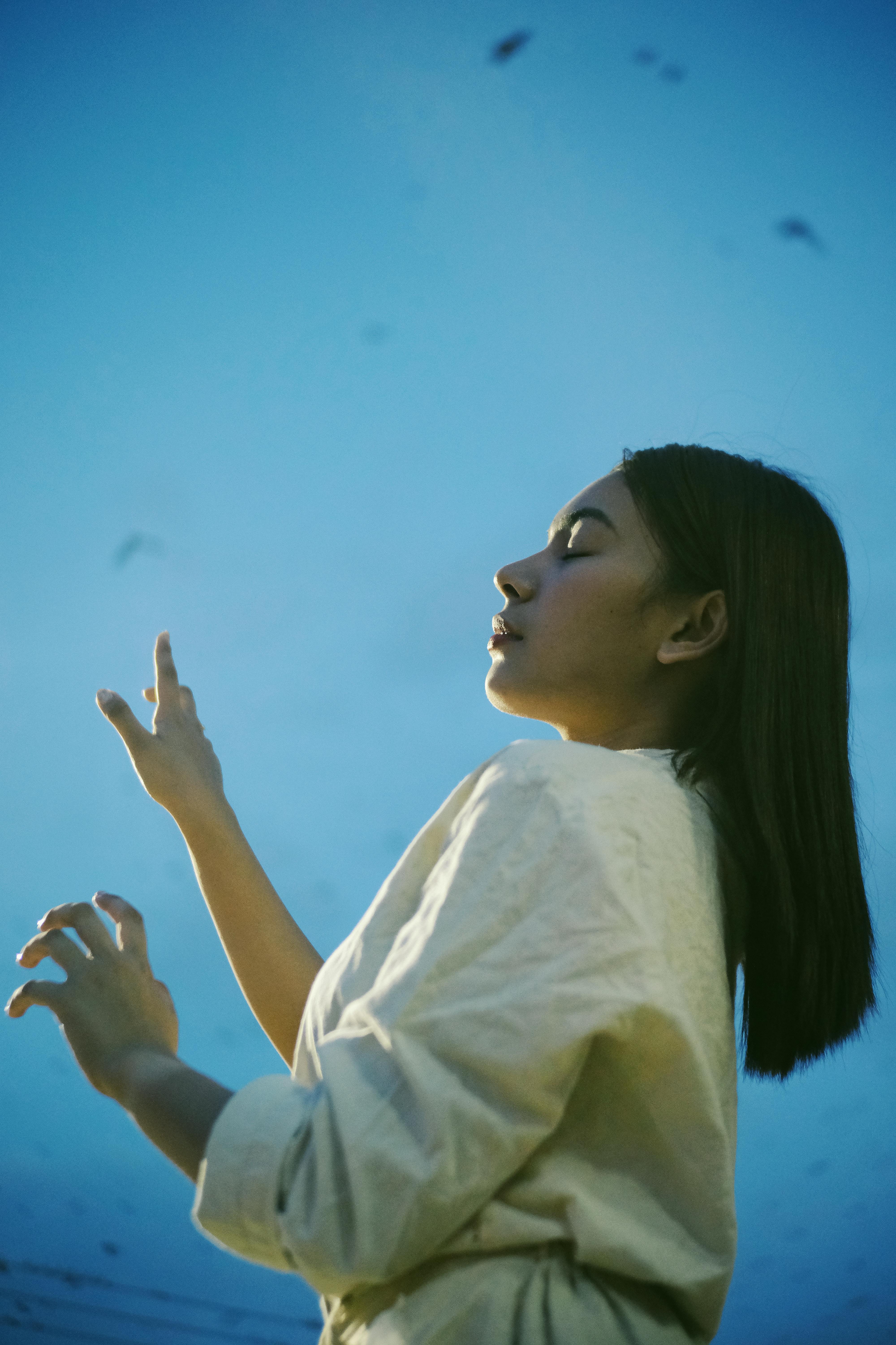 Side view of a woman posing with eyes closed against a blue sky, showcasing casual fashion.