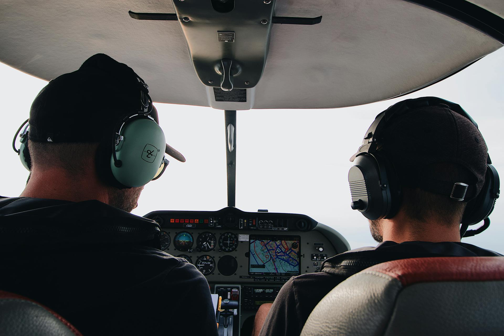 Two pilots with headsets operating controls in an aircraft cockpit.