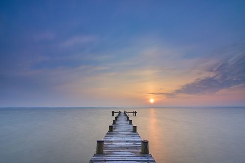 Free Serene sunrise over a tranquil lake with a wooden pier leading into the distance. Stock Photo