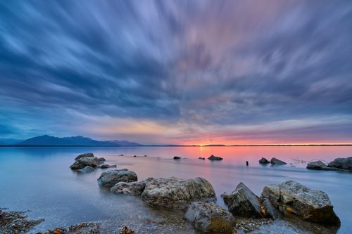 Free Tranquil sunset view over lake in Bavaria, Germany with rocky shoreline and calm waters. Stock Photo