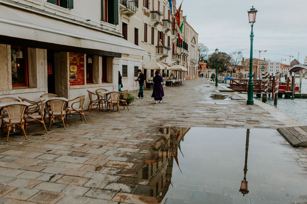 Stradă venețiană lângă canal, cu terase și reflexii după ploaie