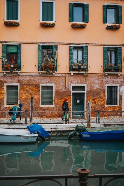 Free Colorful building by a Venetian canal with boats and pedestrians. Stock Photo