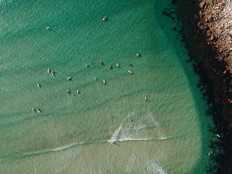 Drone shot capturing canoes scattered on transparent turquoise ocean near rocky shore.