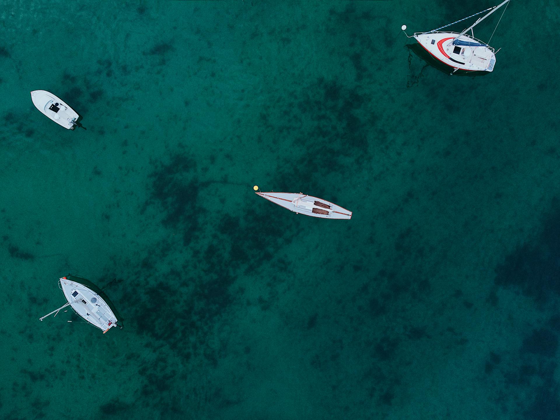 Drone capture of sailboats gently floating on clear blue water, showcasing serene marine travel.
