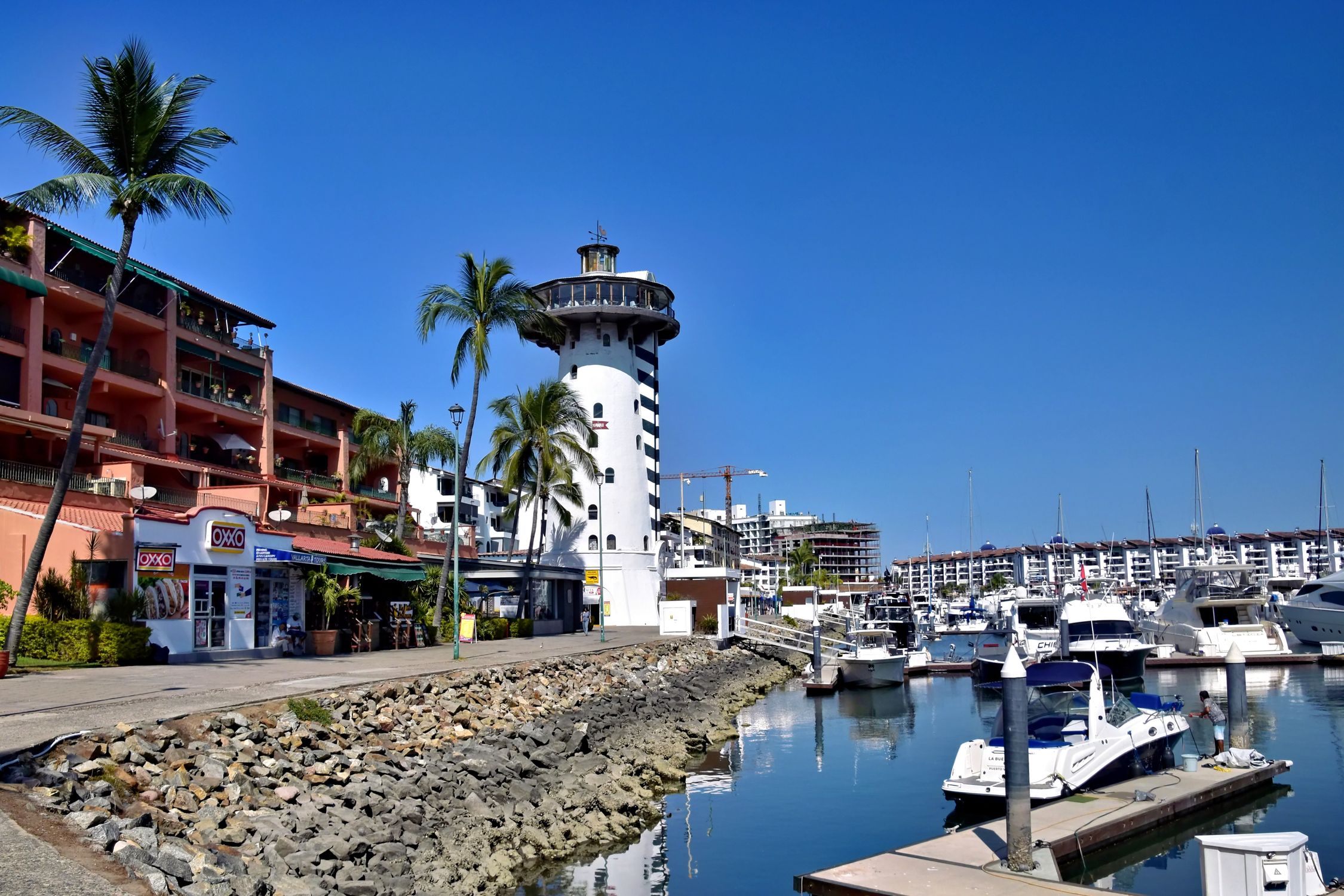 Scenic view of Marina Vallarta lighthouse and waterfront boats under a clear blue sky.
