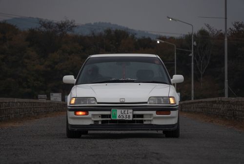 Free Classic white car with headlights on, parked on a country road under dim evening light. Stock Photo