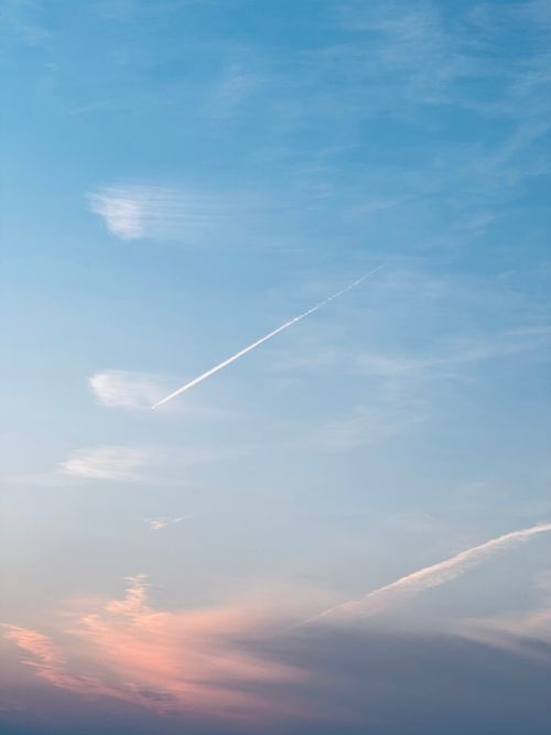 Free Tranquil sky featuring soft clouds and a distinct airplane contrail during sunset. Stock Photo