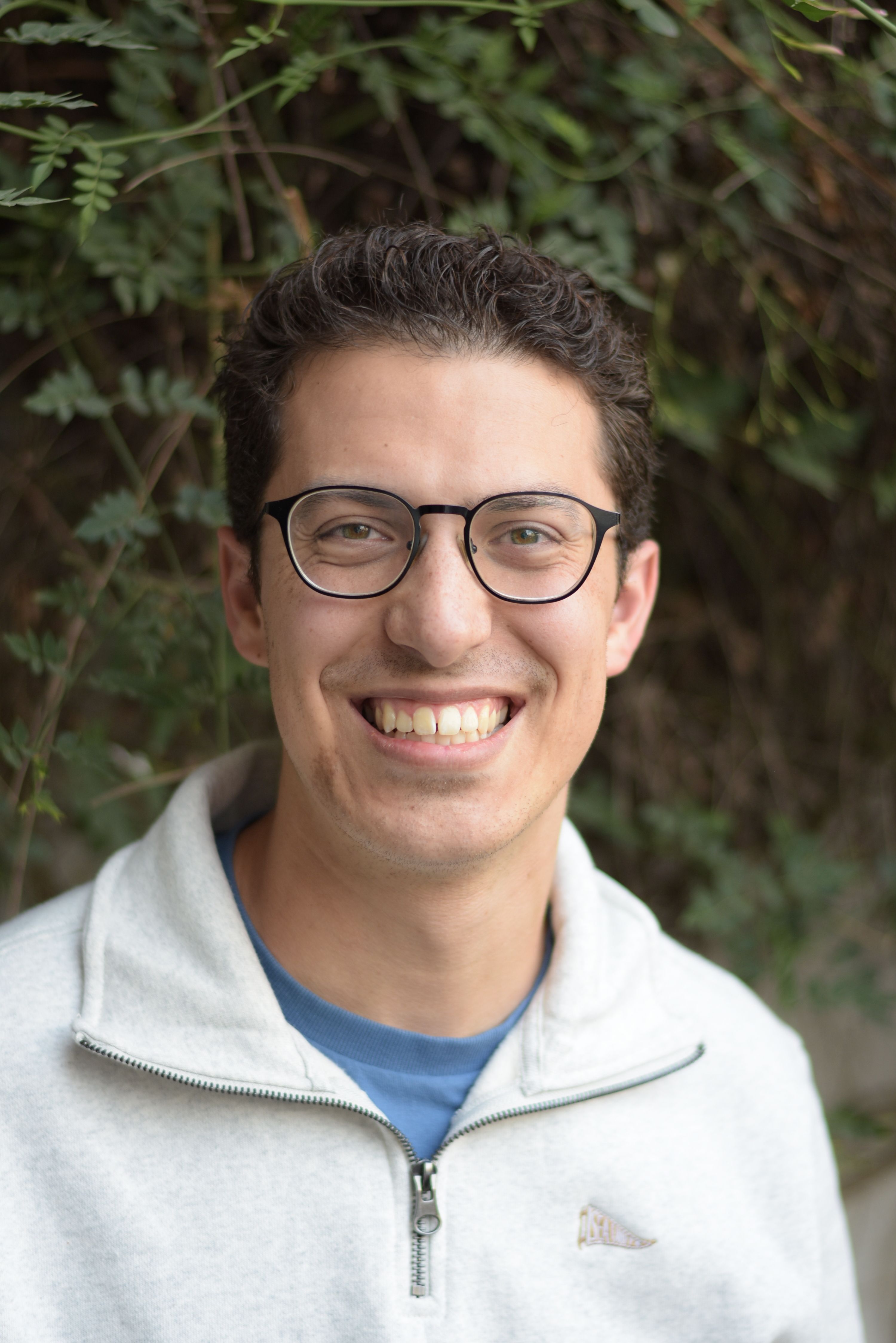 Portrait of a smiling man with glasses against lush greenery in Mexico.