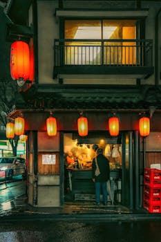 Nighttime street view of a traditional Japanese eatery in Tokyo with red lanterns and customers.