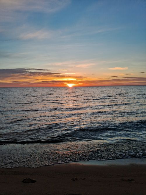 Free Stunning sunset over calm sea with vibrant colors and gentle waves on a sandy beach. Stock Photo