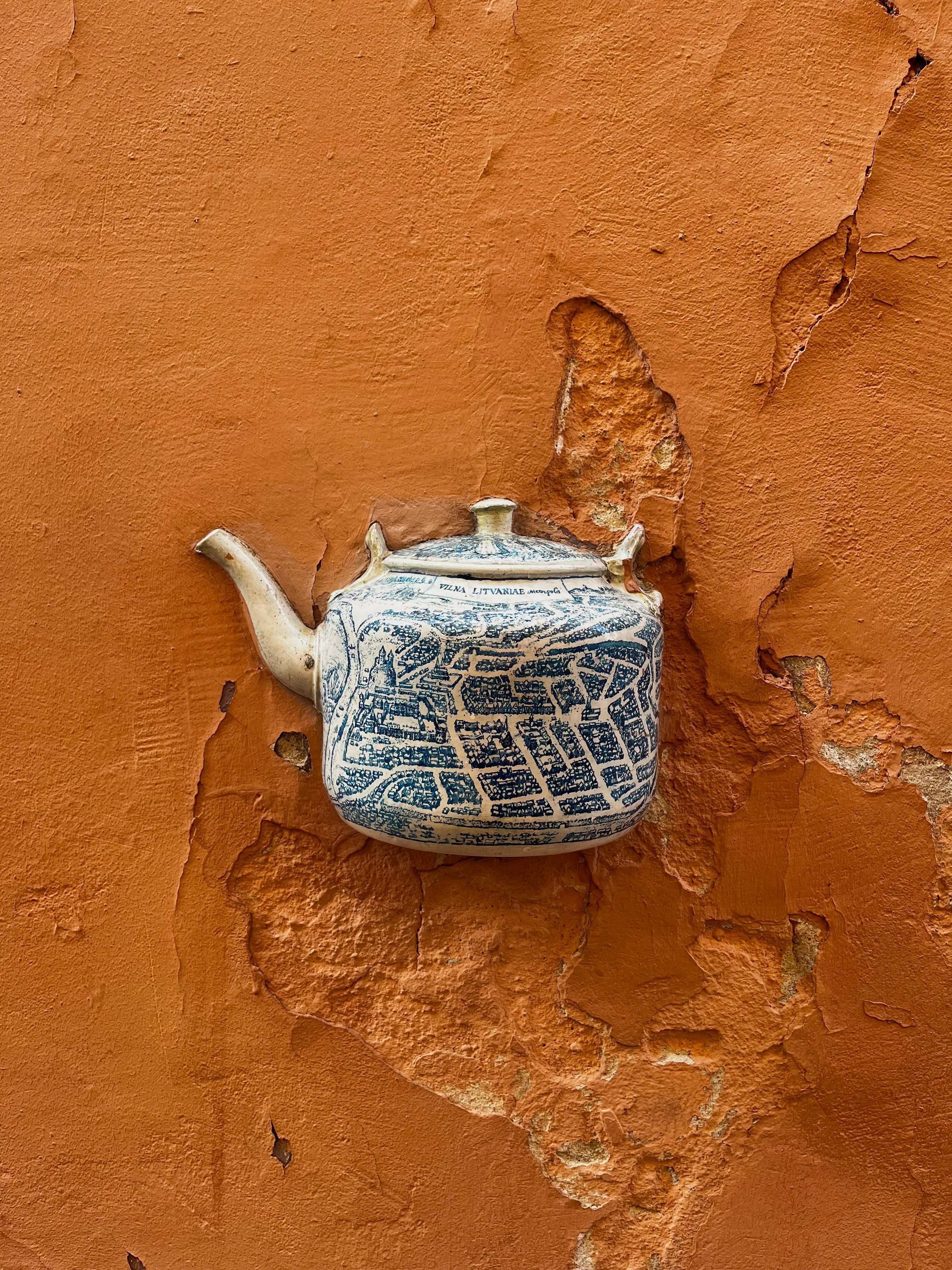 Detailed street art of a vintage teapot map on a weathered terracotta wall in Vilnius, Lithuania.