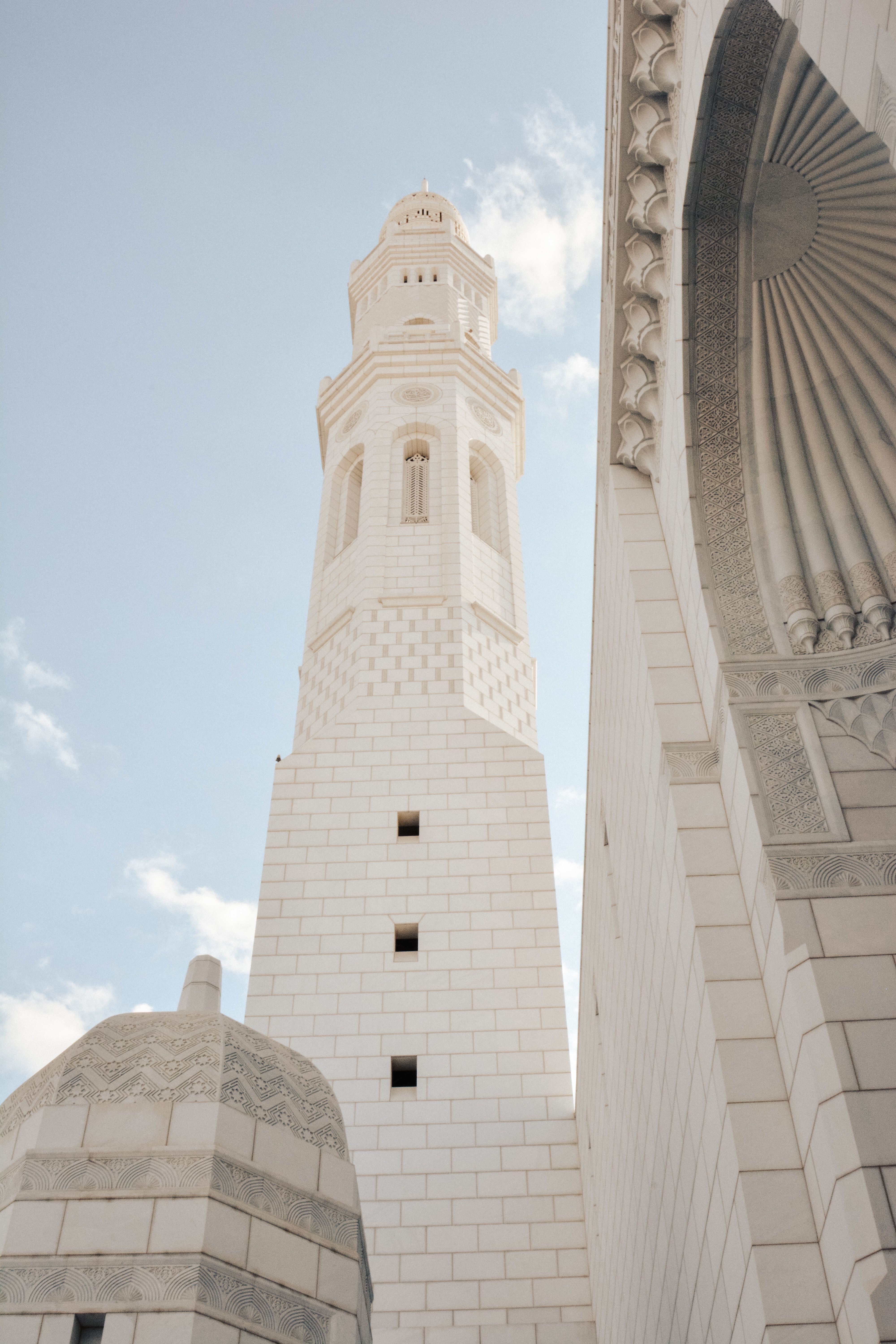A stunning view of the minaret of Sultan Qaboos Grand Mosque in Muscat, Oman against a blue sky.