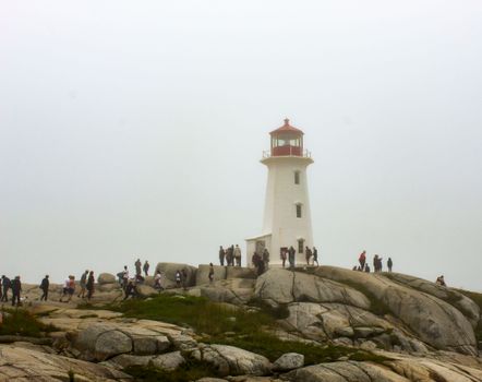 Tourists explore Peggy's Cove Lighthouse on a misty day in Nova Scotia.