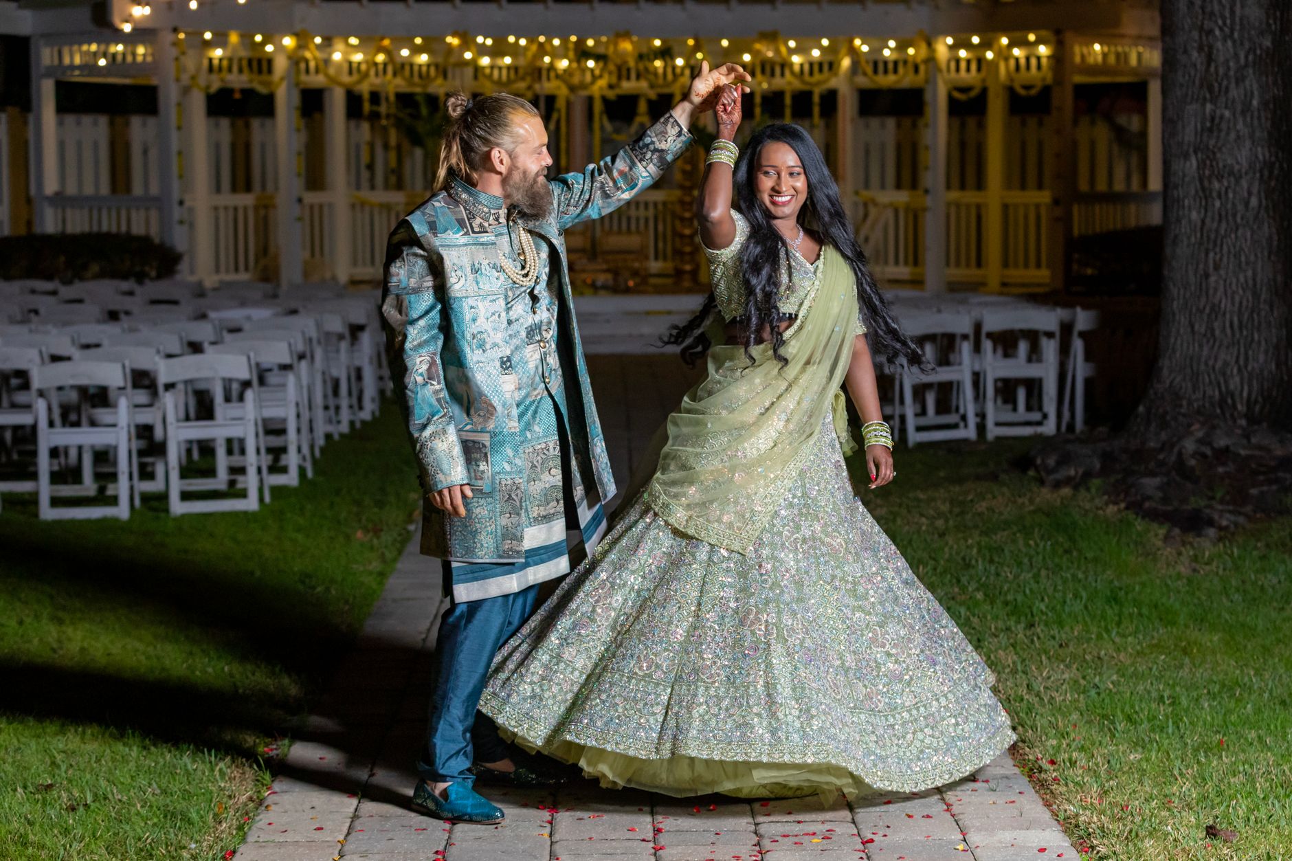 Happy couple celebrating their wedding with a dance under string lights outdoors at night.