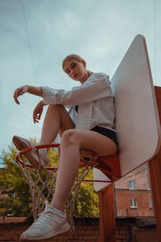 A young woman casually sits on a basketball hoop, embodying youthful rebellion.
