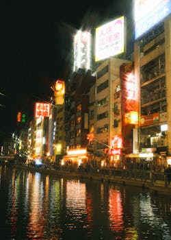 Lively night scene in Dotonbori, Osaka with neon lights reflecting on the river.