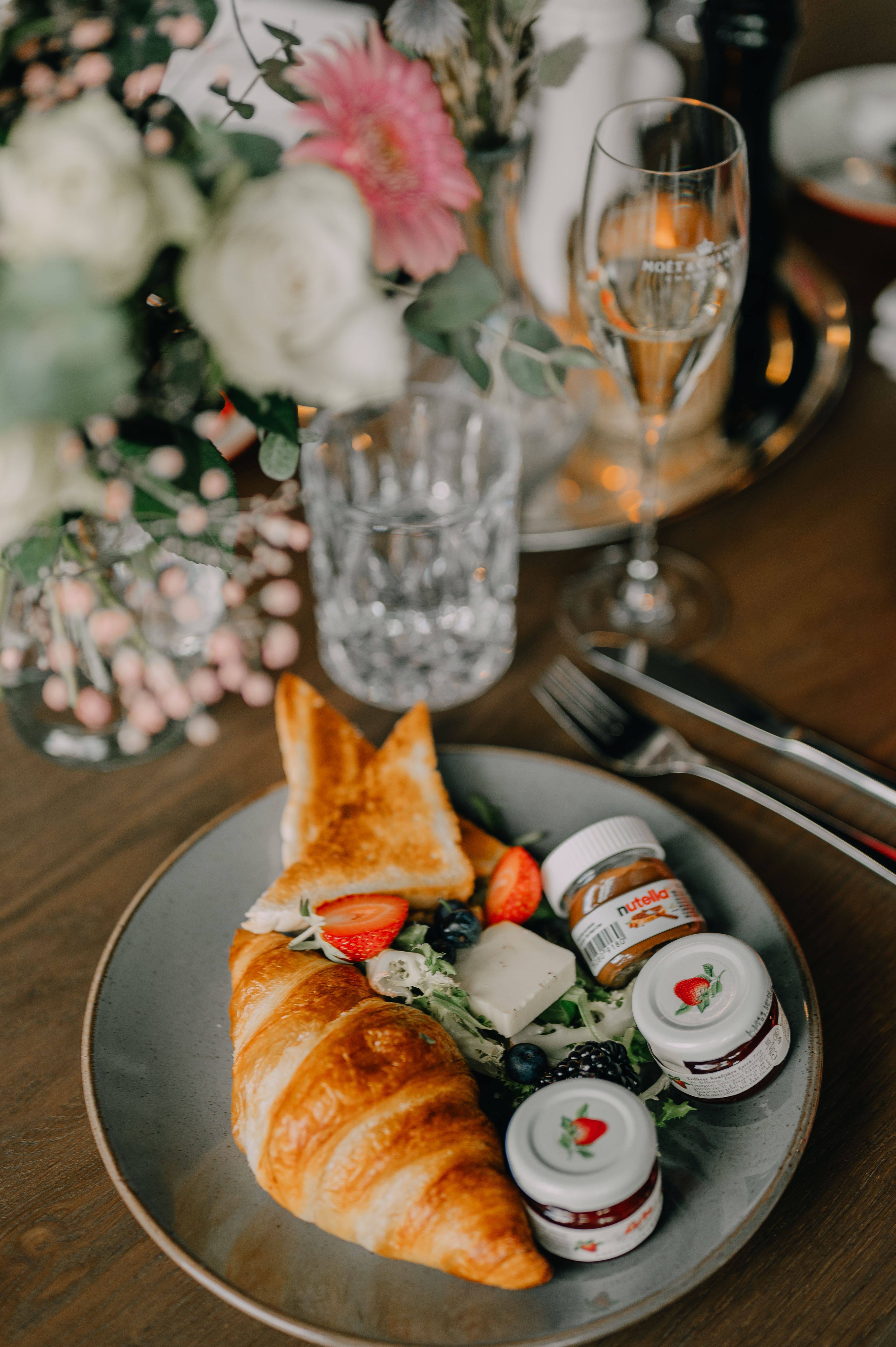 A gourmet breakfast setting featuring a croissant, jam, and fresh fruits on a wooden table.