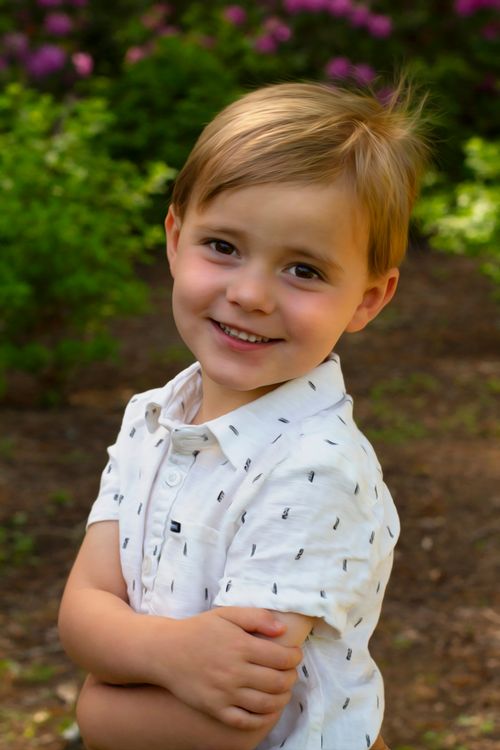Free Charming portrait of a blond boy smiling in a sunny outdoor setting. Stock Photo