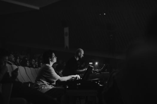 Monochrome photo of concert technicians and audience in a dimly lit theater.