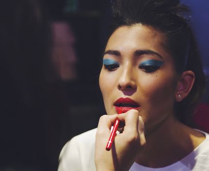 A makeup artist applies bold lip color to an Asian model. Shot in England.