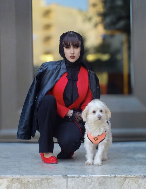 Free Stylish woman in red with a dog posing outdoors against a blurred urban backdrop. Stock Photo