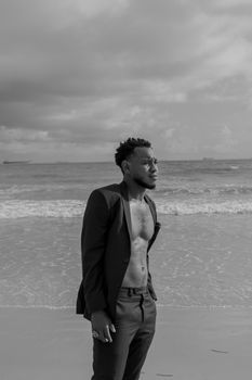 A man in a suit stands thoughtfully by the ocean, captured in black and white.