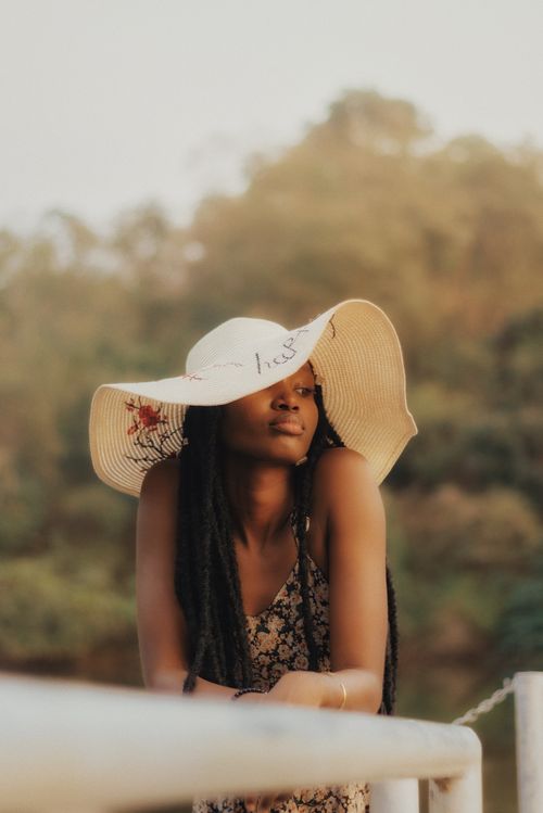 Free A stylish woman in a sundress and hat leaning on a railing in Abuja, Nigeria, at sunset. Stock Photo