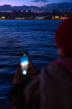 Capturing a city skyline at twilight with a blurred person holding a mobile phone in the foreground.