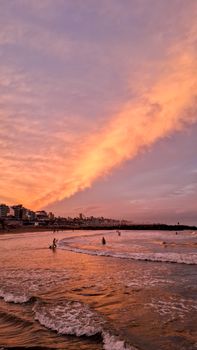 Silhouette of people at the beach during a vibrant sunset with city skyline.