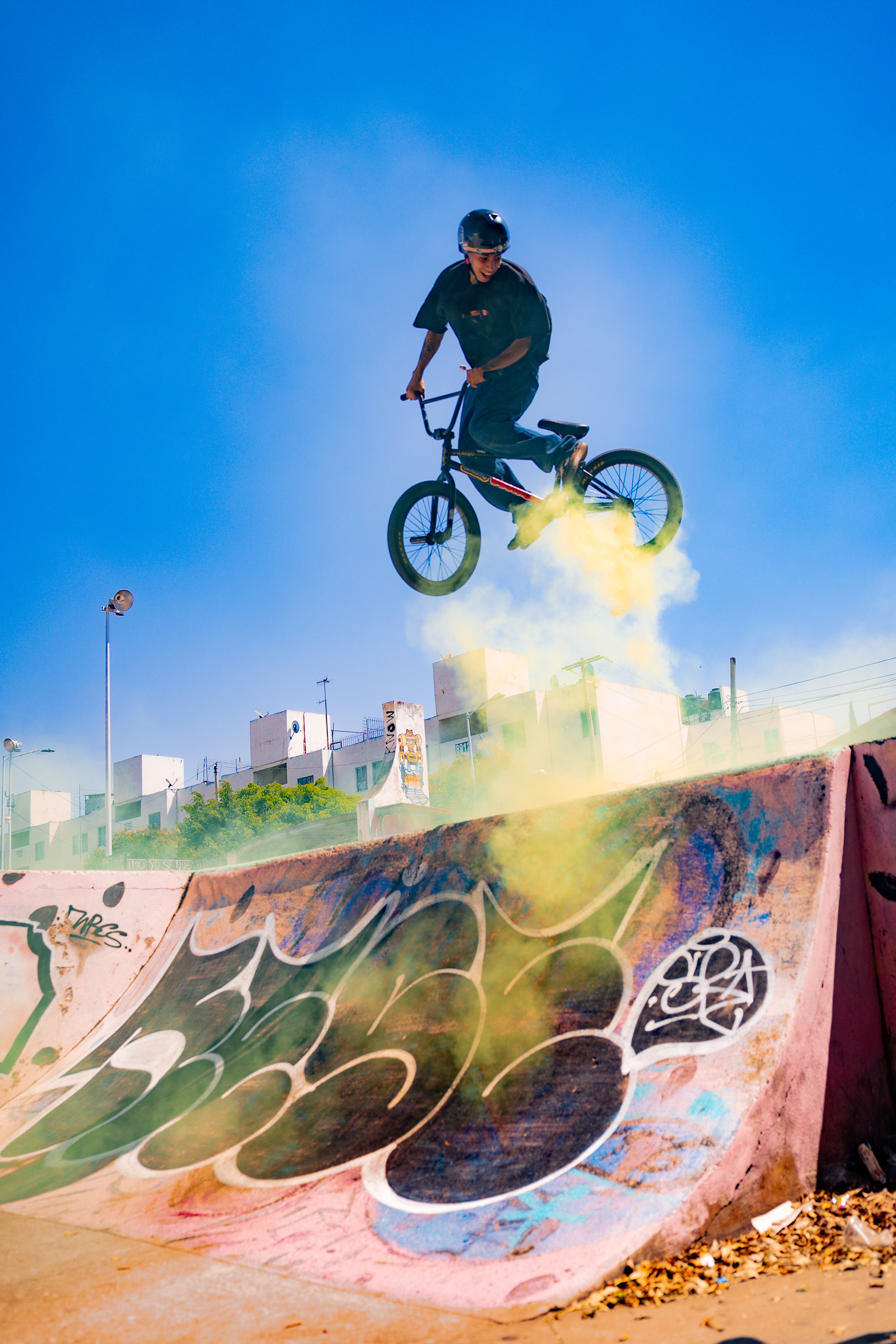 BMX cyclist executes high-flying stunt in vibrant urban skatepark with colorful smoke effect.