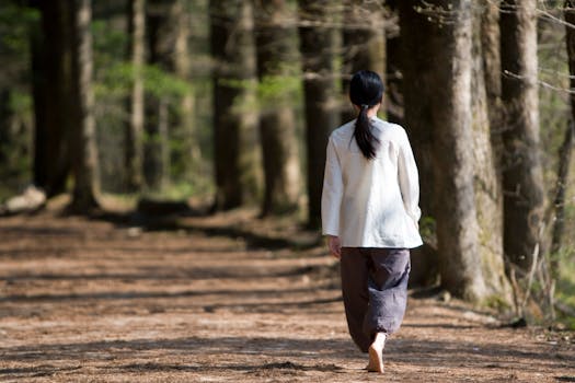 A woman walks barefoot along a peaceful forest path under sunlight, reflecting tranquility.