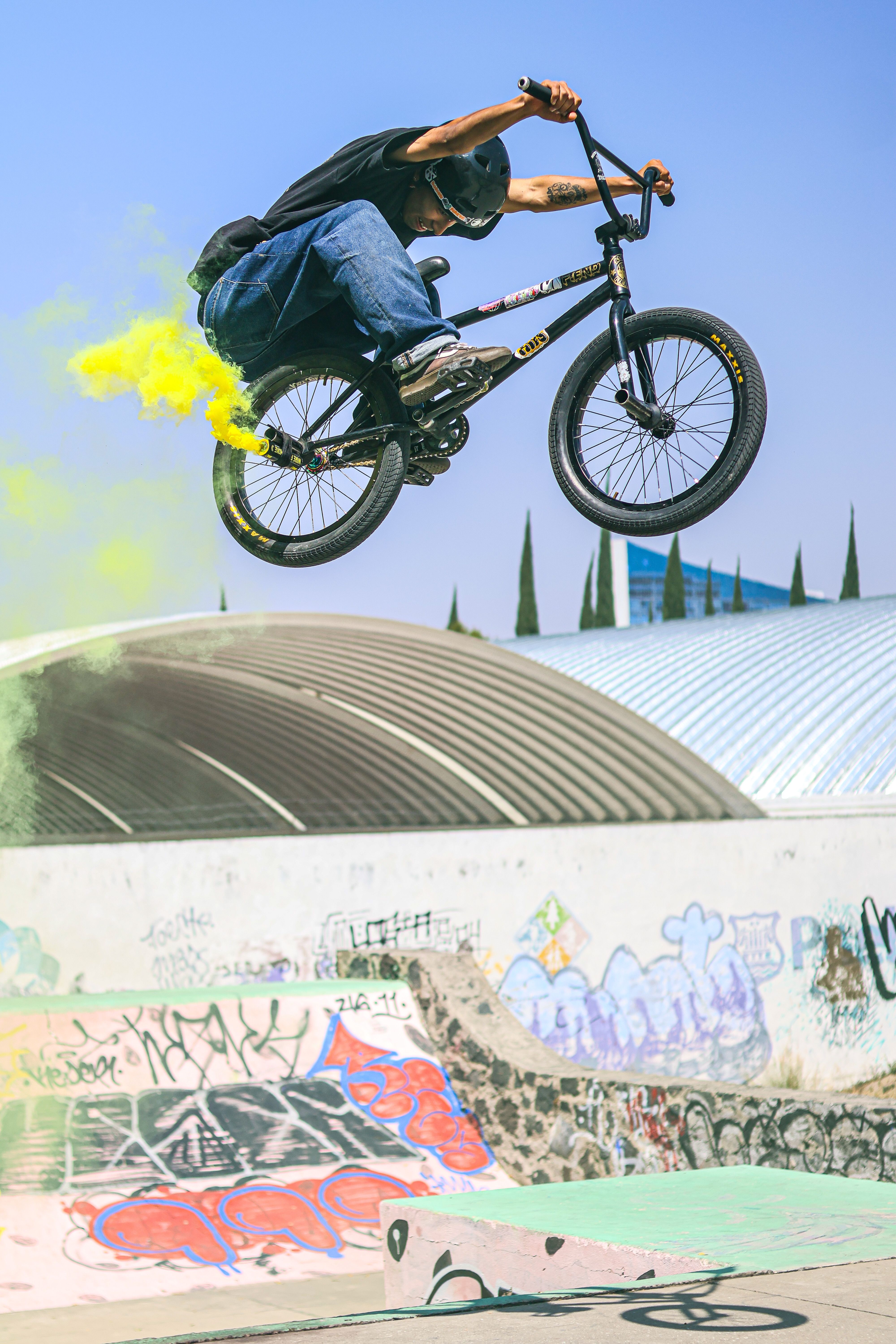 BMX rider performs a high-flying trick with vibrant smoke at urban skate park.